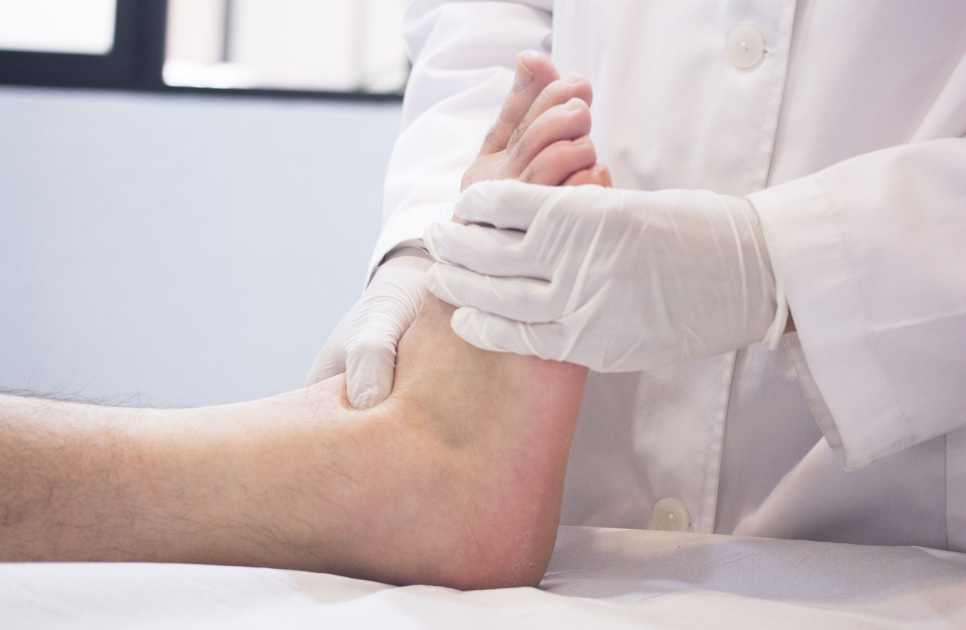 Doctor's gloved hands examining a patient's foot on a white surface.