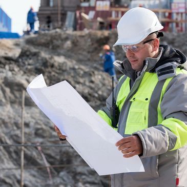 A man wearing a hard hat and safety vest is looking at a blueprint.