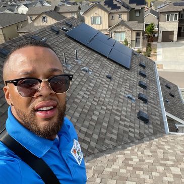 A man wearing sunglasses is standing on top of a roof with solar panels.