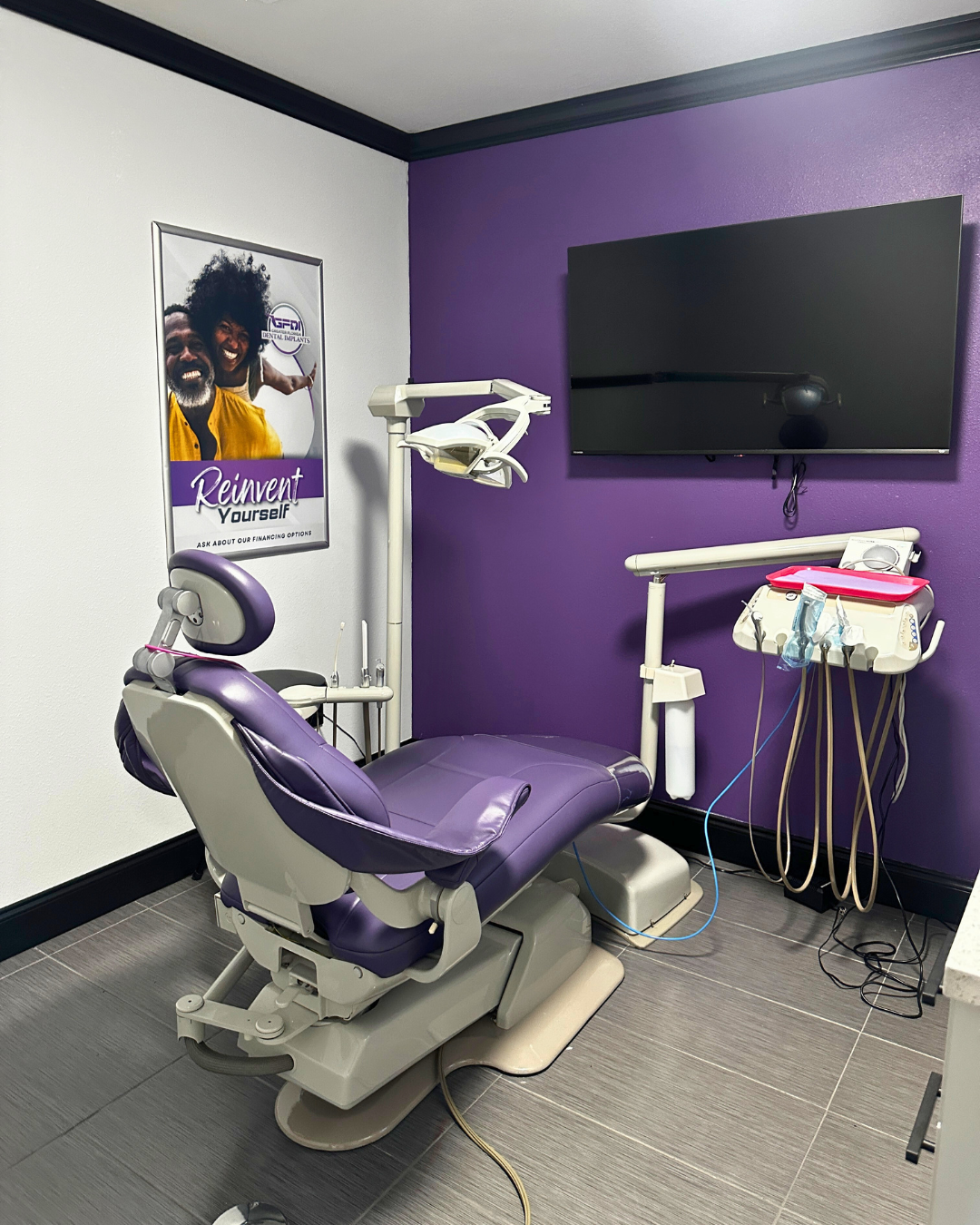 Purple dental chair in an exam room, with dental equipment and a TV on the wall.