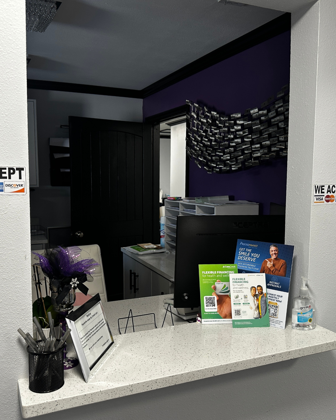 Reception desk with a speckled countertop, brochures, and a computer. Purple and black wall in the background.