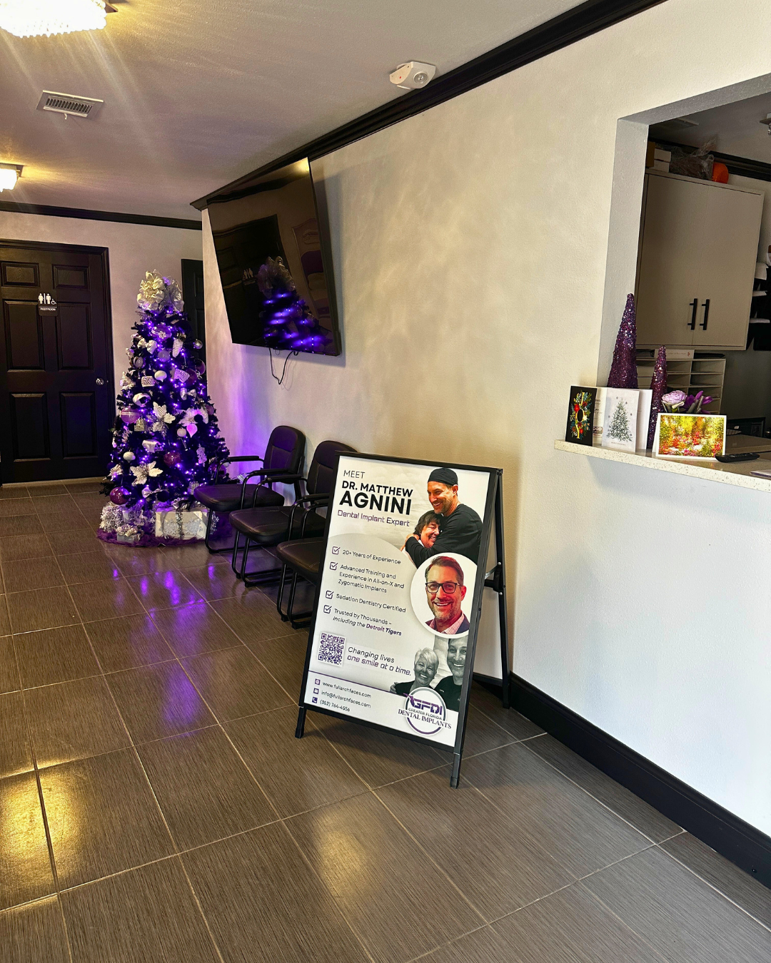 Waiting area with Christmas tree, seating, sign advertising a person, and television.