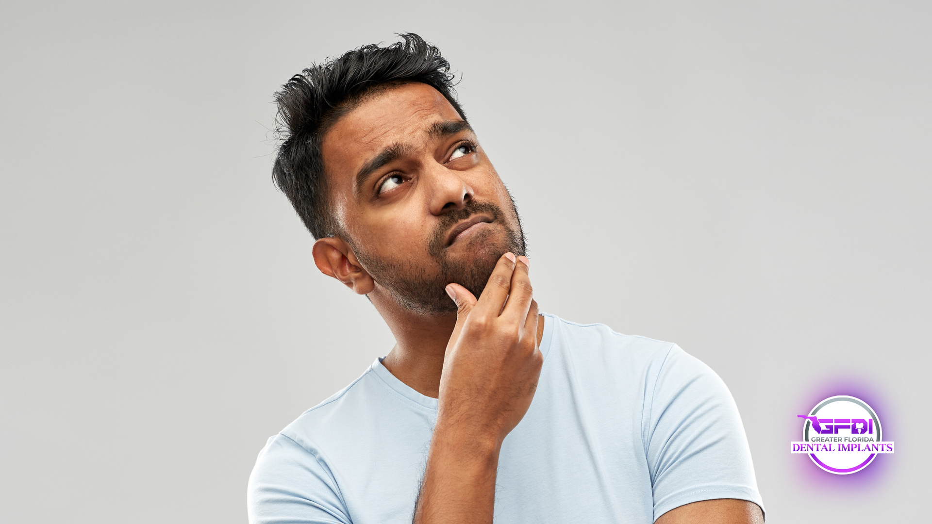 Man in light blue shirt, hand on chin, looking upward with a thoughtful expression.