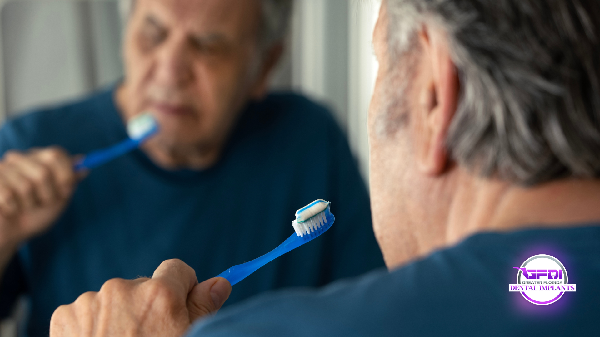 Man brushing teeth in front of a mirror, using blue toothbrush.