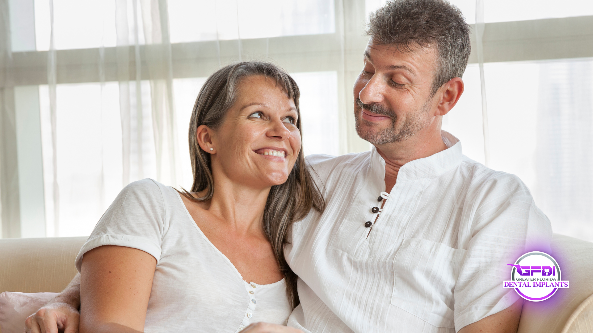 Smiling older couple, man with hand on woman's shoulder, posing against a white background.