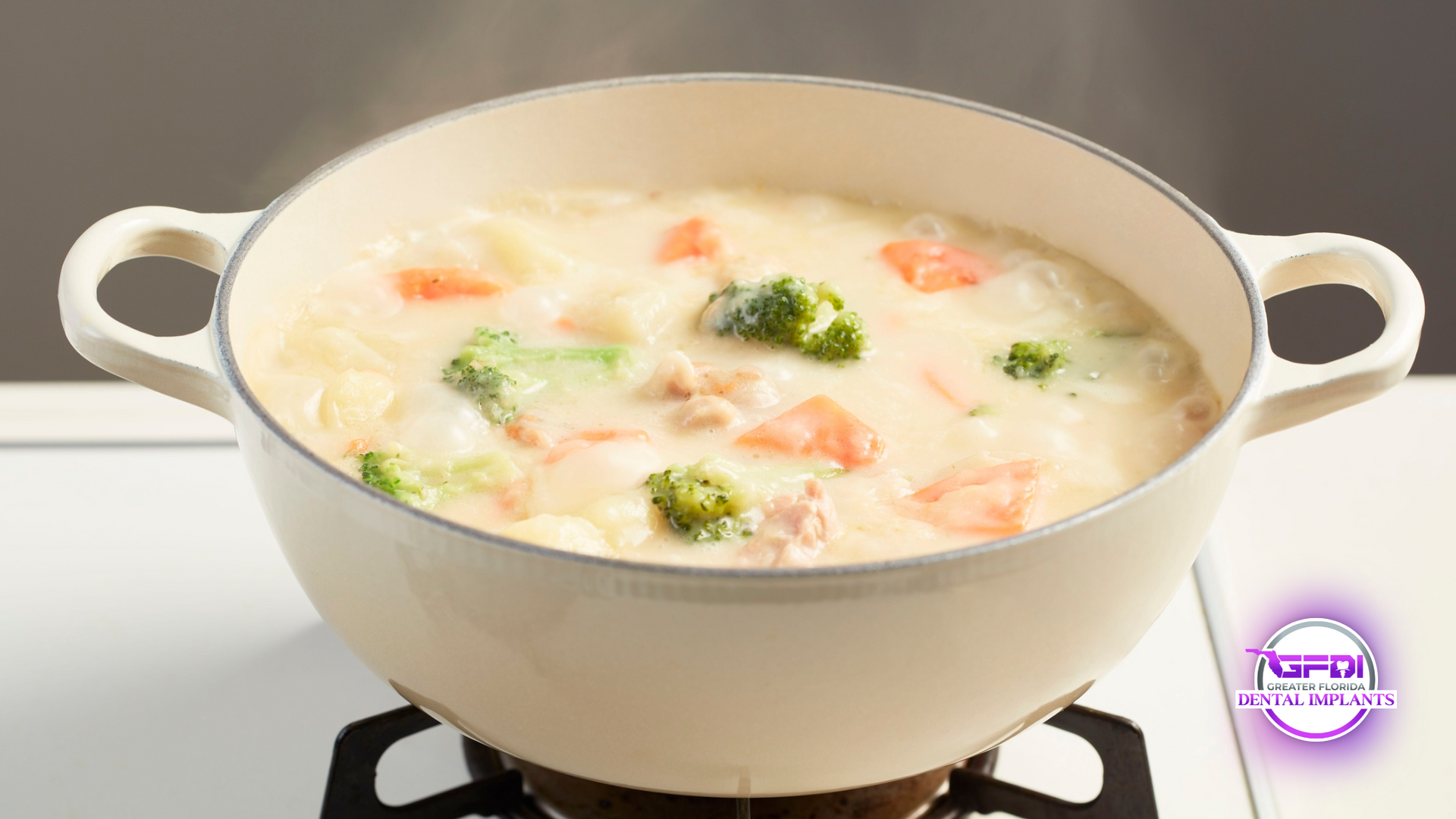 White pot on stove with steaming creamy stew including broccoli, carrots, and potatoes.