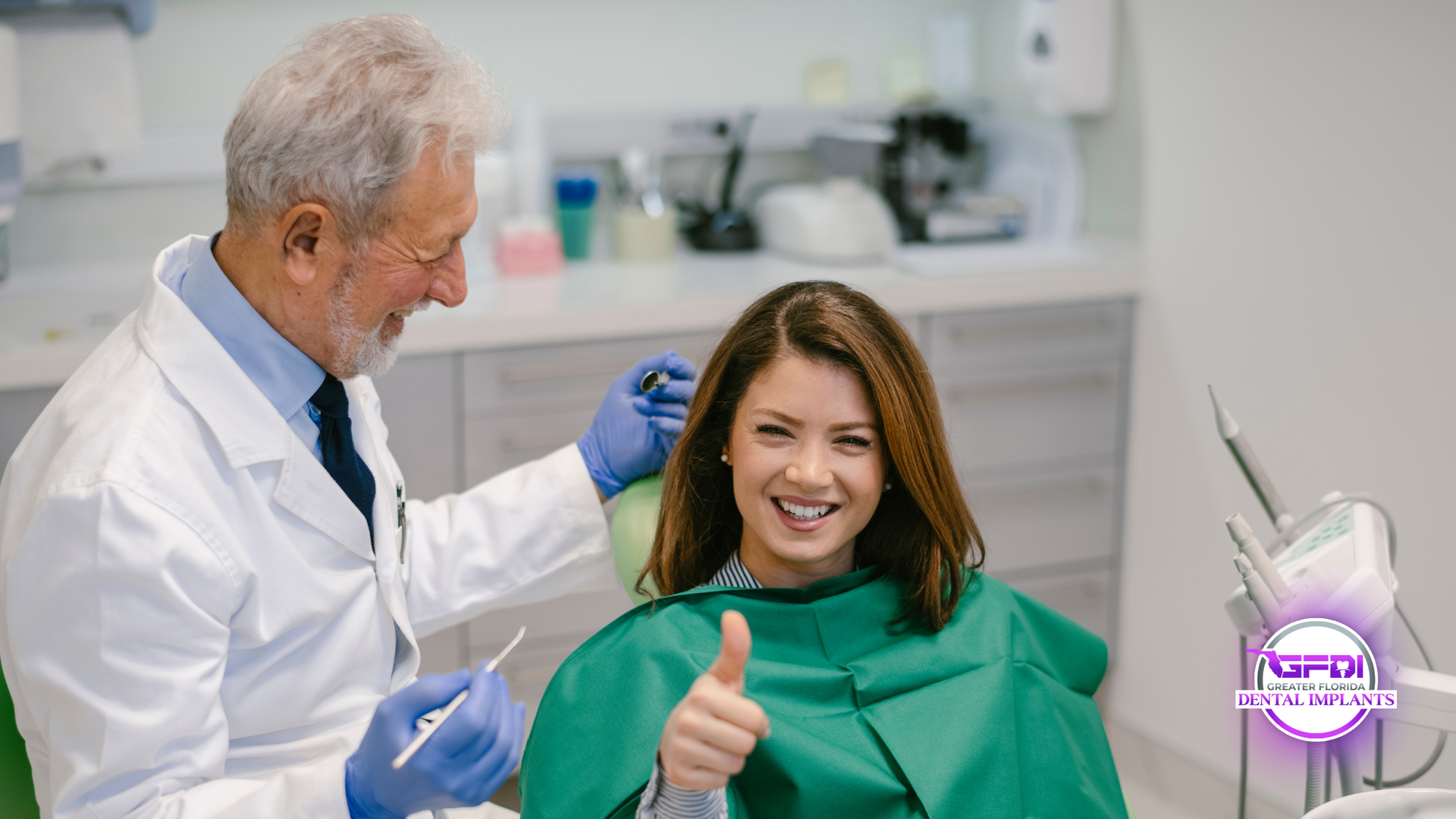 Dentist smiling next to a woman in a dental chair, giving a thumbs up. In a dental office.