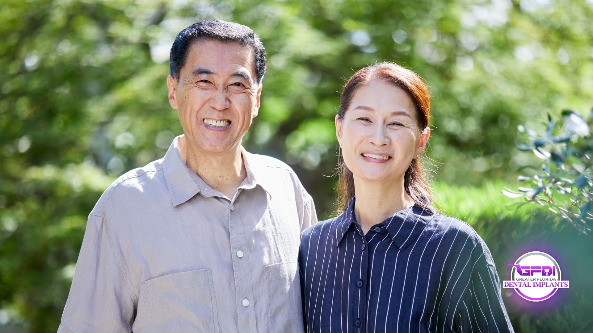 Smiling couple in front of greenery, man in light shirt, woman in striped shirt.