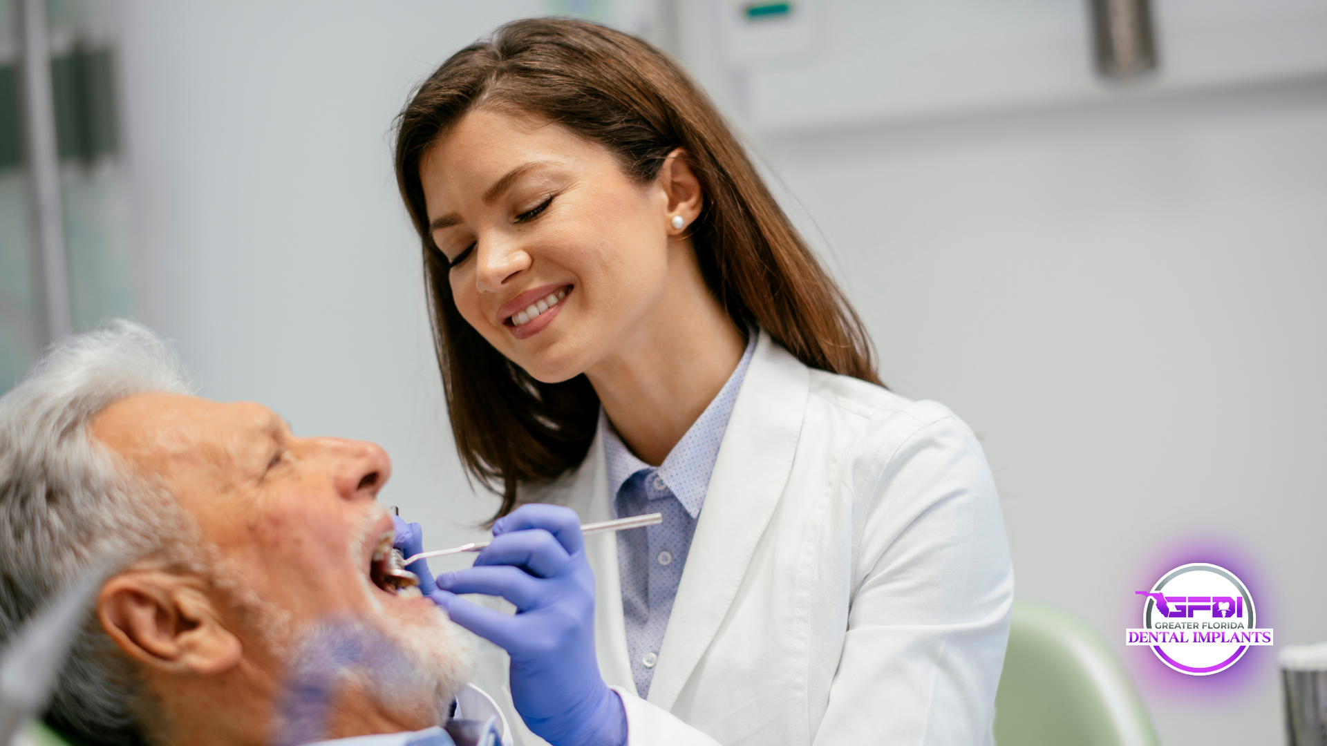 A smiling dentist examines an elderly patient's teeth in a dental office.