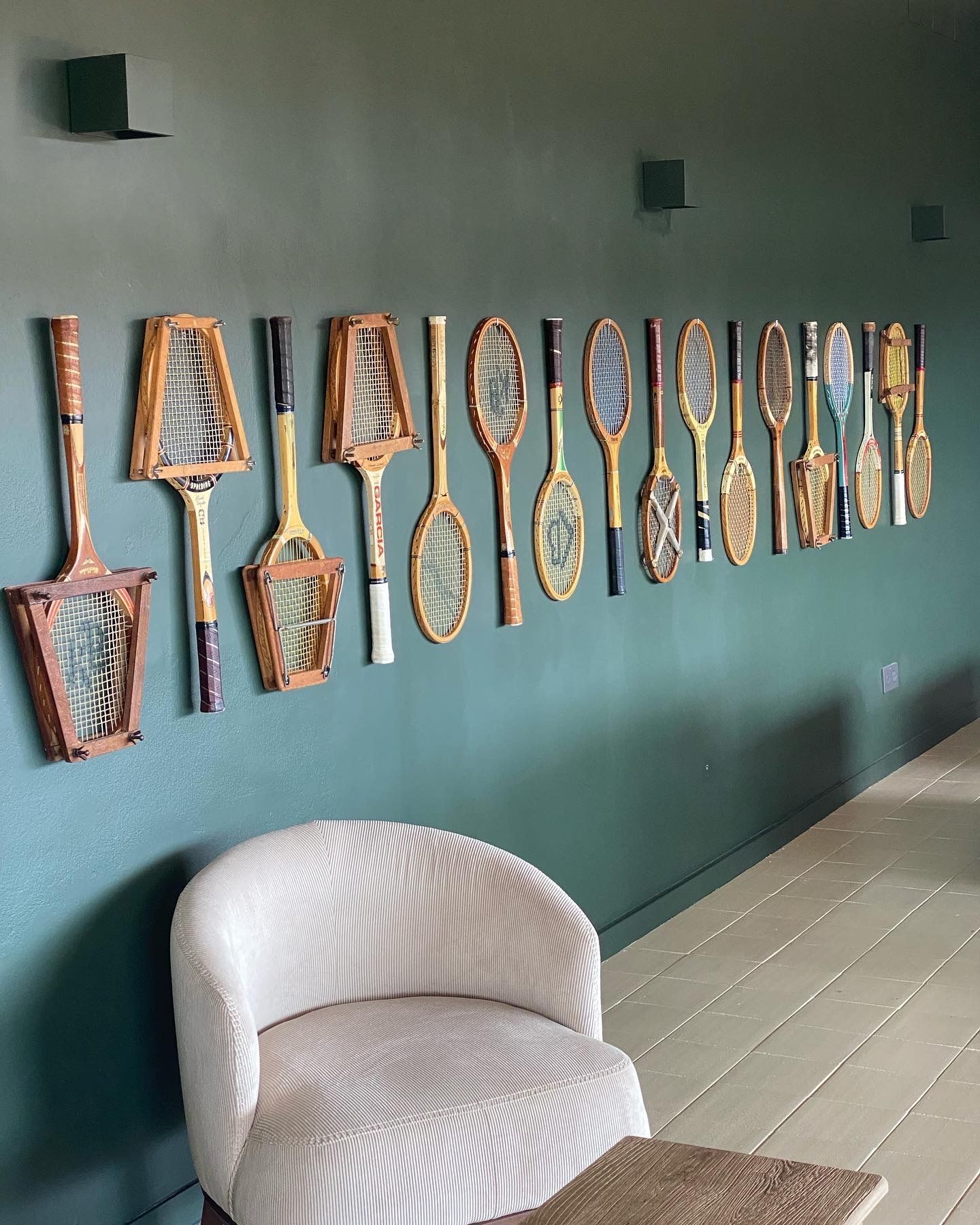 Una fila de raquetas de tenis colgadas en una pared al lado de una silla.