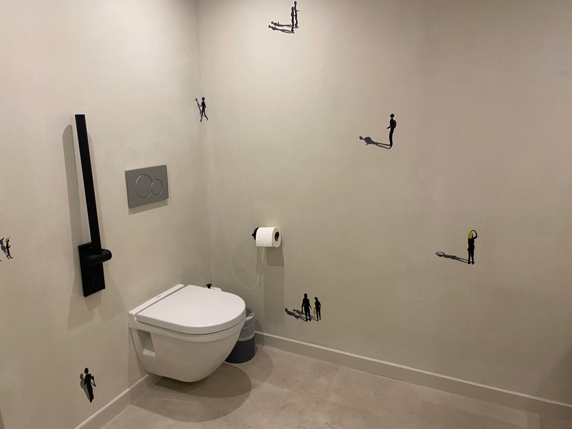 Un baño con inodoro, bote de basura y ganchos en la pared.