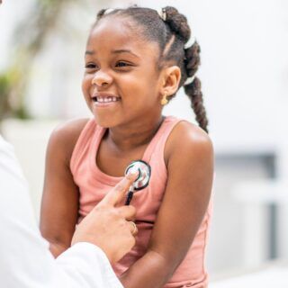 Doctor listens to a child's chest with a stethoscope. The child smiles in a medical office.