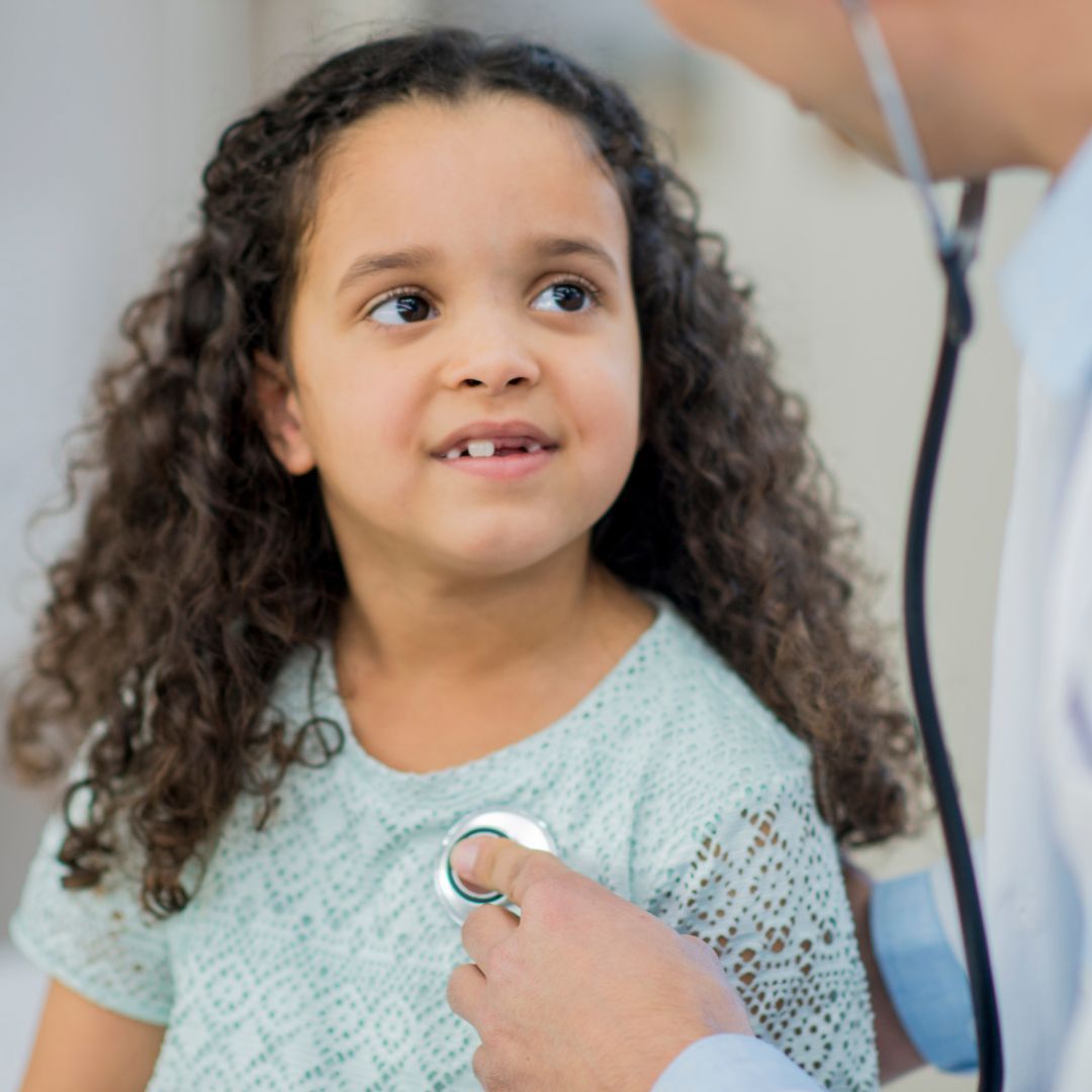 Girl in a light blue shirt listens to a doctor's stethoscope during a checkup.