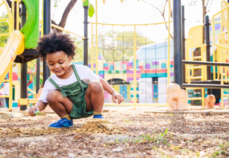 A young boy is squatting in the dirt at a playground.