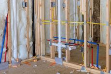 Framed walls of a room under construction with plumbing, electrical wiring, and insulation visible.