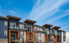 Multi-story townhomes with balconies under a blue sky. Exterior is blue, gray, and wood.