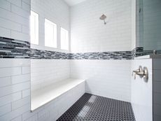 White tiled bathroom with a built-in bench, shower head, and black hexagon tiled floor.