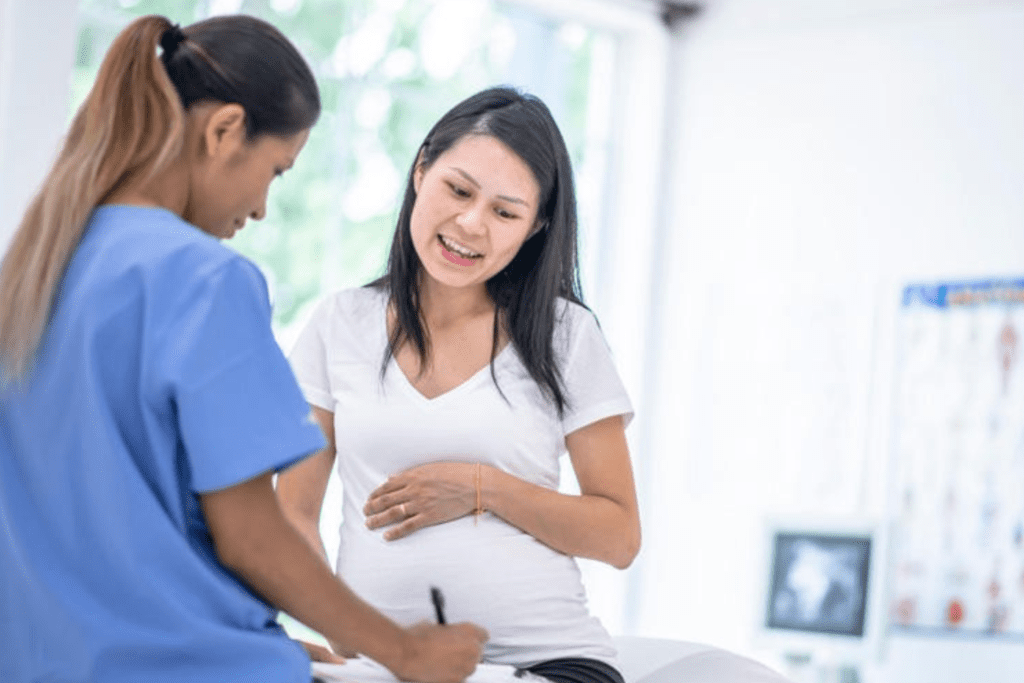 Nurse in blue scrubs consulting with a pregnant patient in a clinic setting.