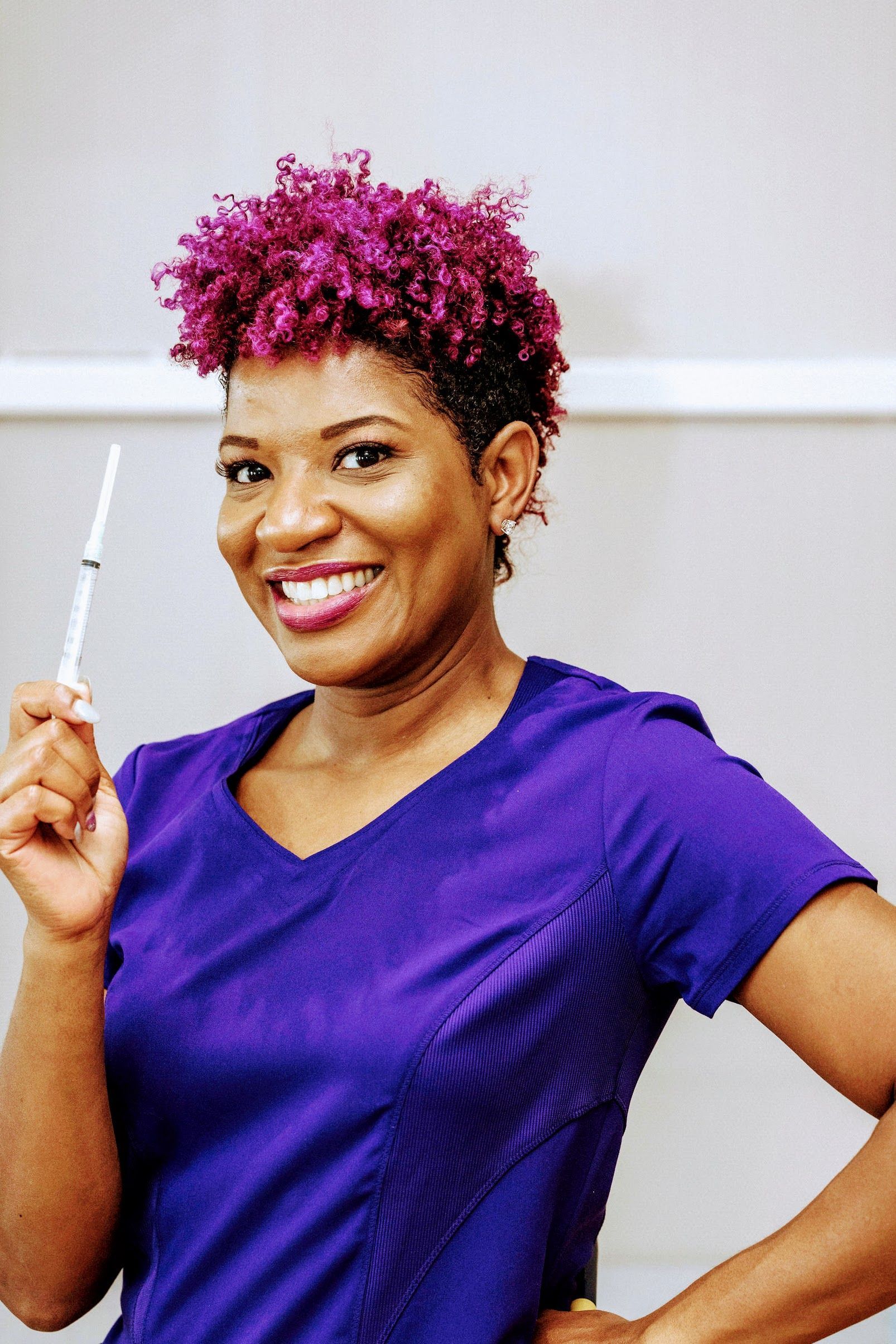 Takera Mitchel, a purple hair and scrubs smiling, holding a syringe.