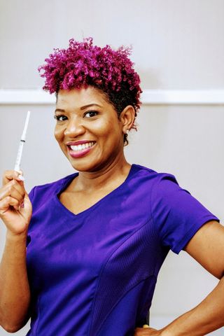 Takera Mitchel, a purple hair and scrubs smiling, holding a syringe.