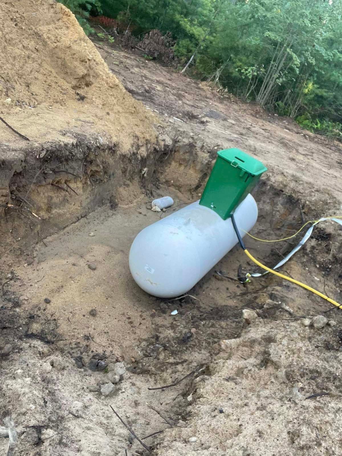 A propane tank is sitting in the dirt next to a pile of dirt.