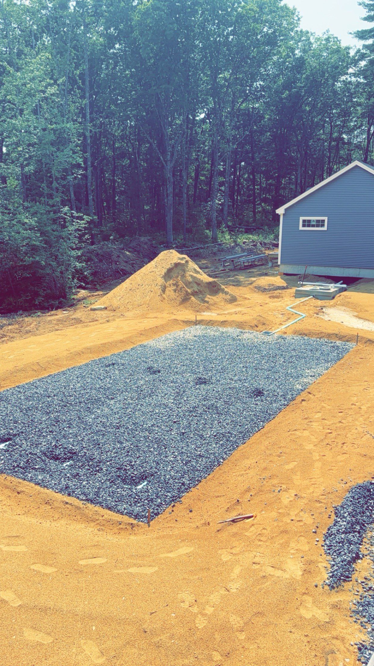 A large pile of gravel is sitting in the middle of a dirt field next to a house.