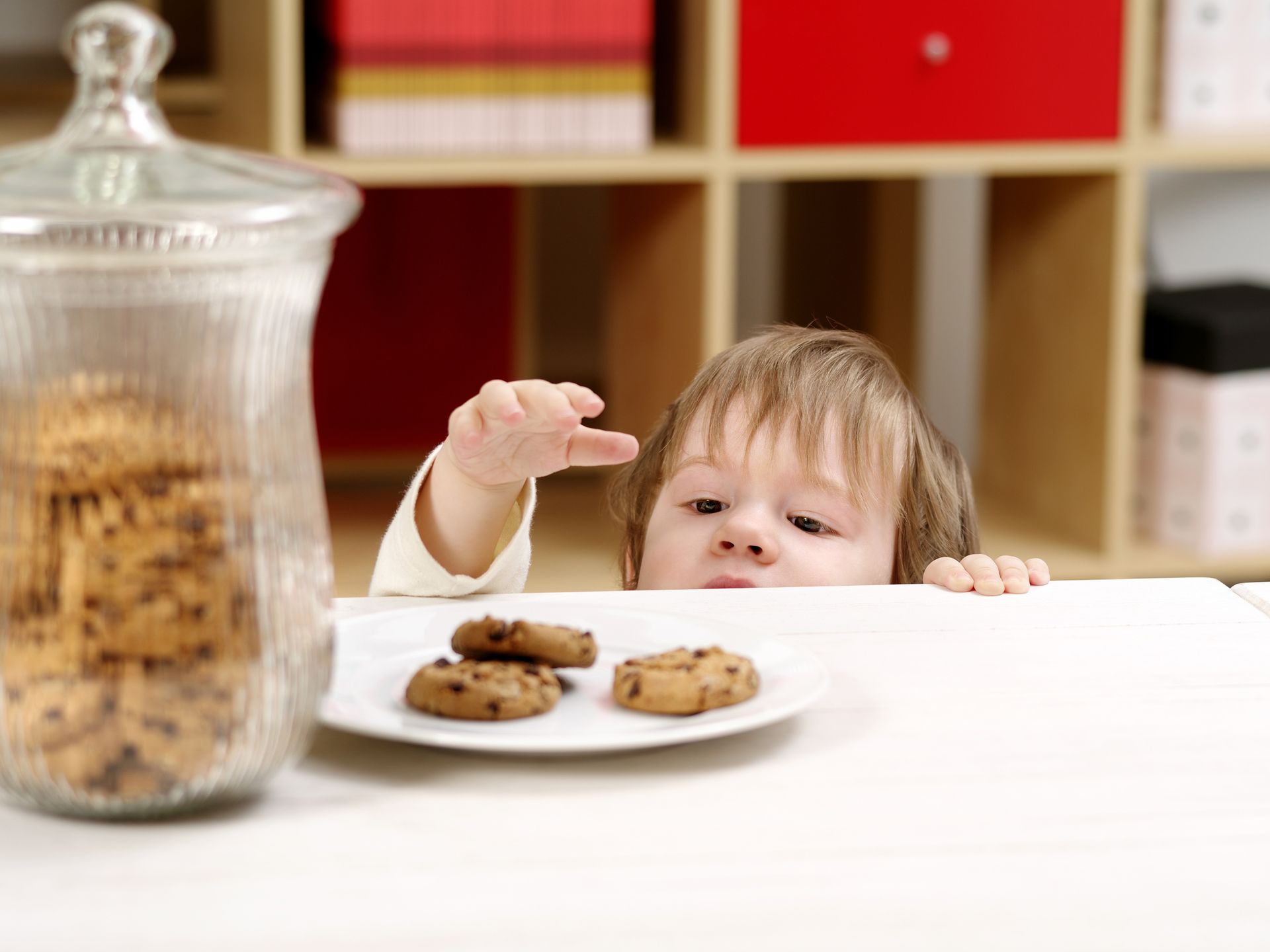Child reaching for a cookie on a plate, jar of cookies beside them.