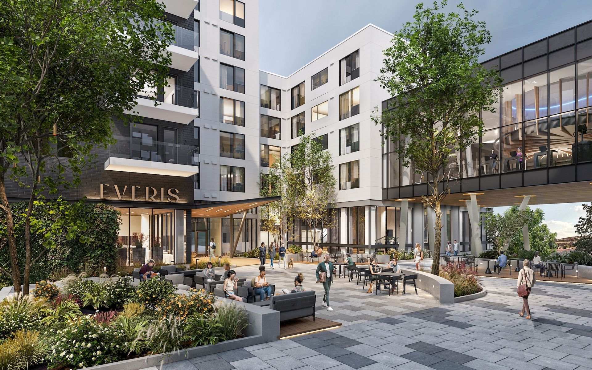 Modern apartment courtyard with trees, seating, flower beds, and people walking near storefronts