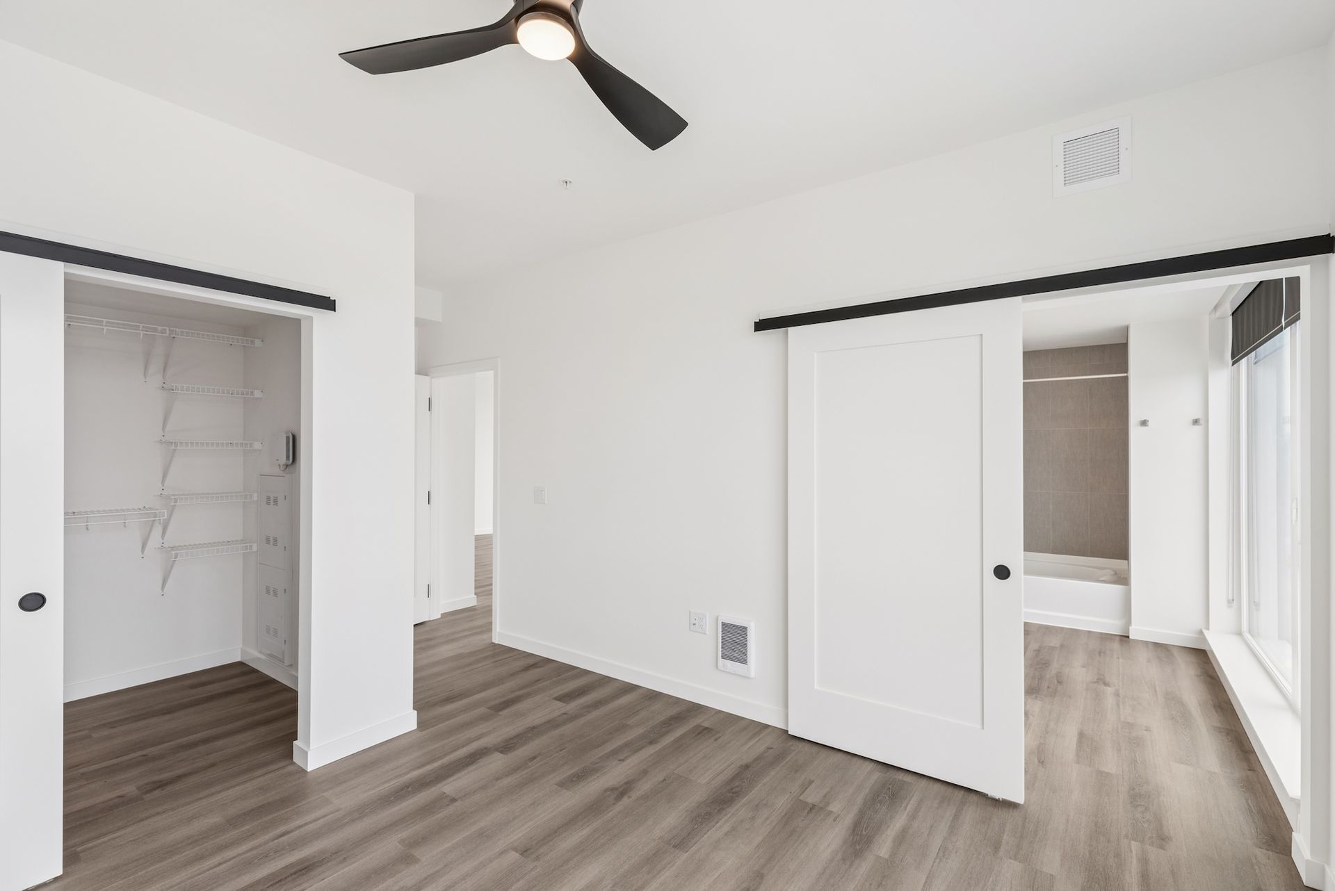 Empty white bedroom with gray wood floors, ceiling fan, and open closet doors
