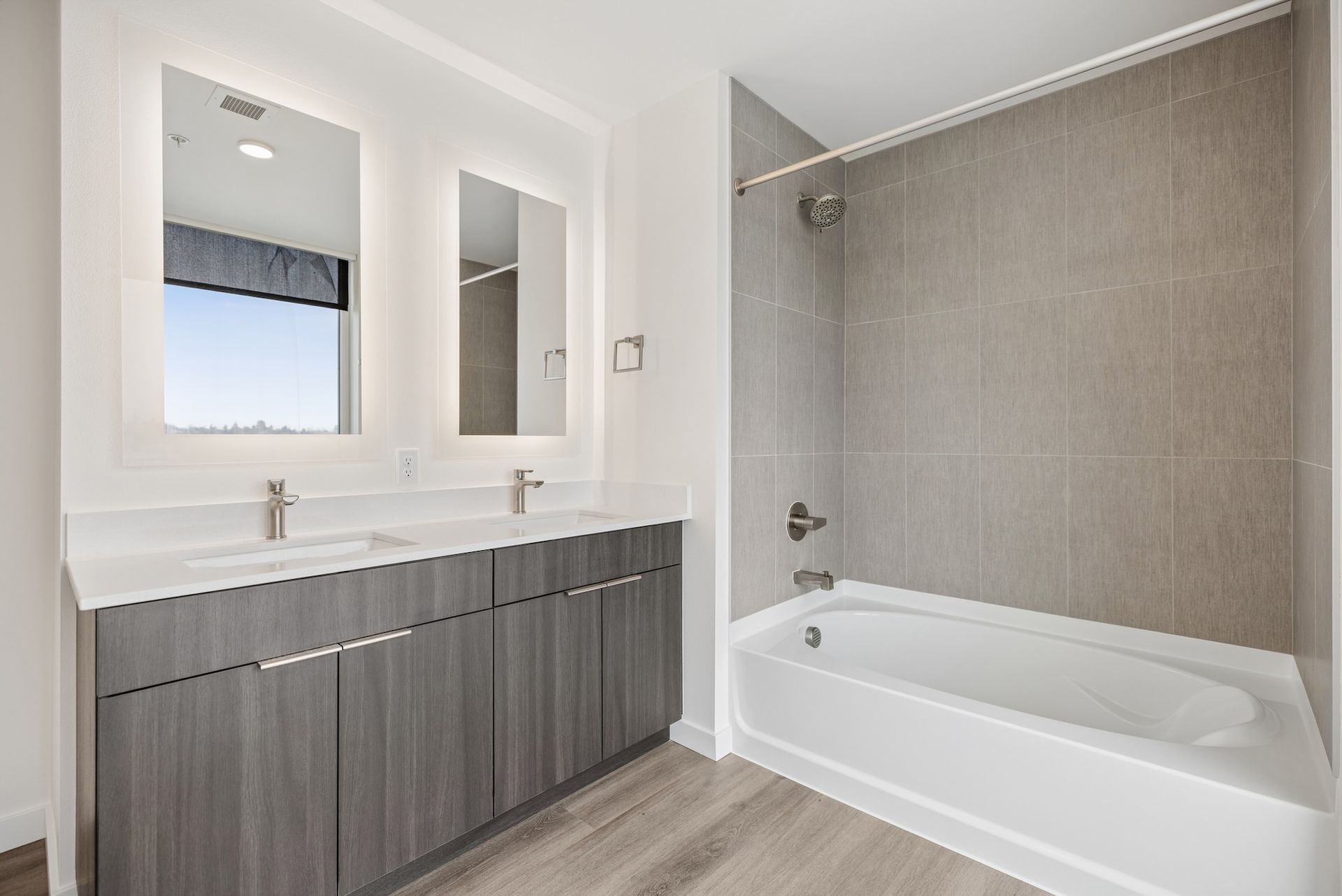 Modern bathroom with double vanity, large mirror, and bathtub with tiled shower surround