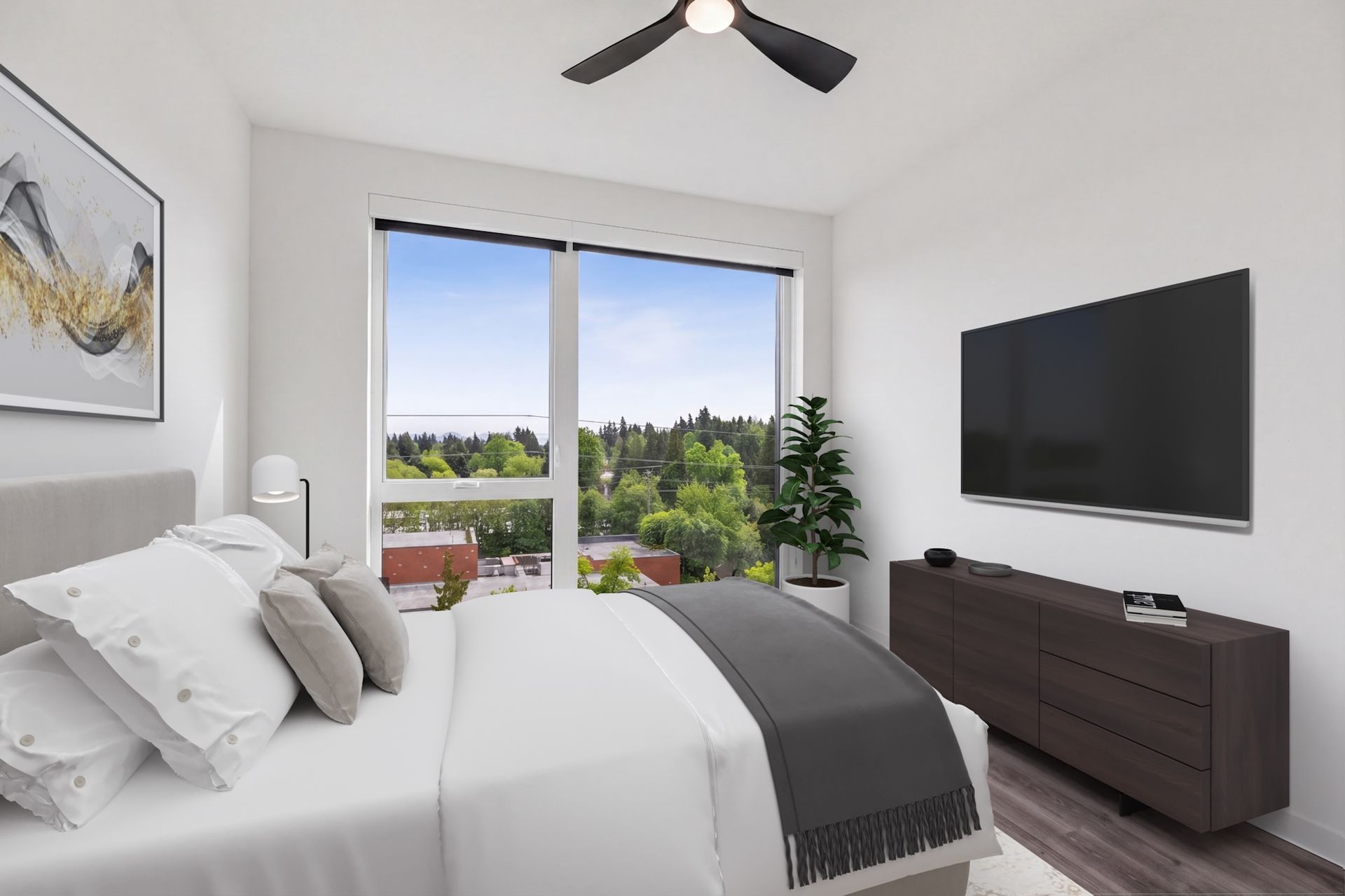 Bright bedroom with white bedding, wall-mounted TV, dresser, and large window overlooking greenery.