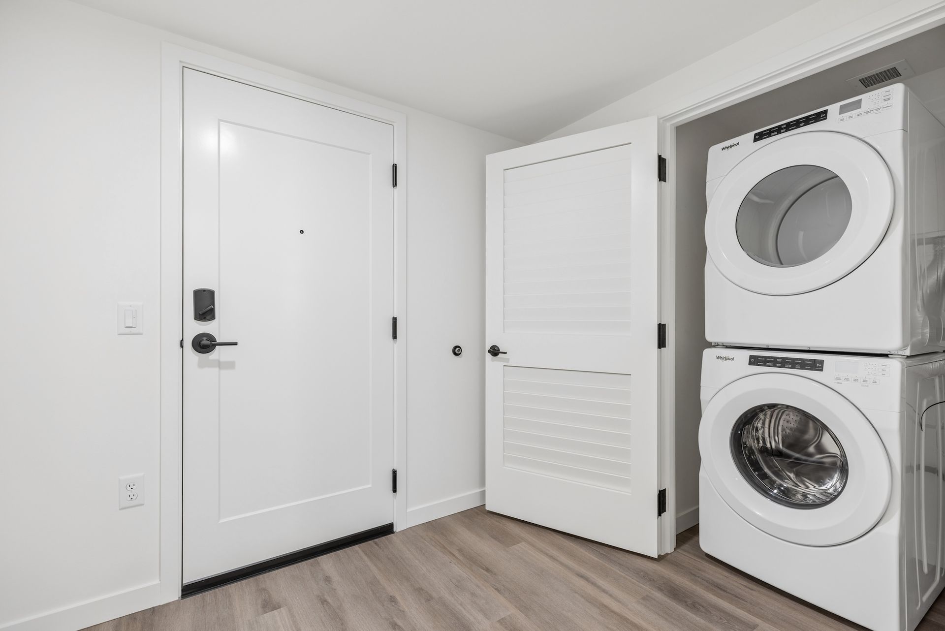 Laundry room with stacked washer and dryer beside a white door and louvered closet door