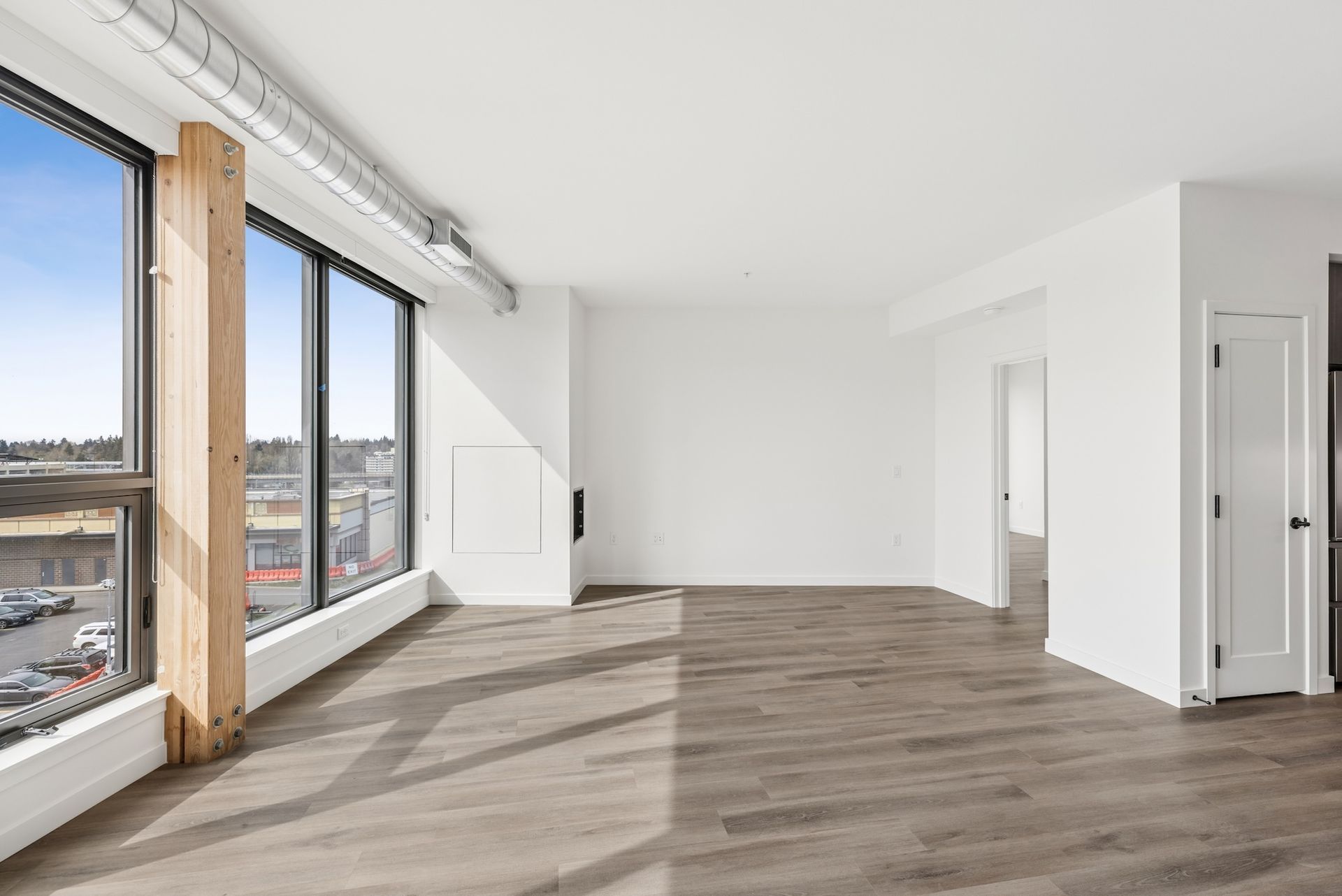 Bright empty apartment with large windows, wood floors, and white walls.
