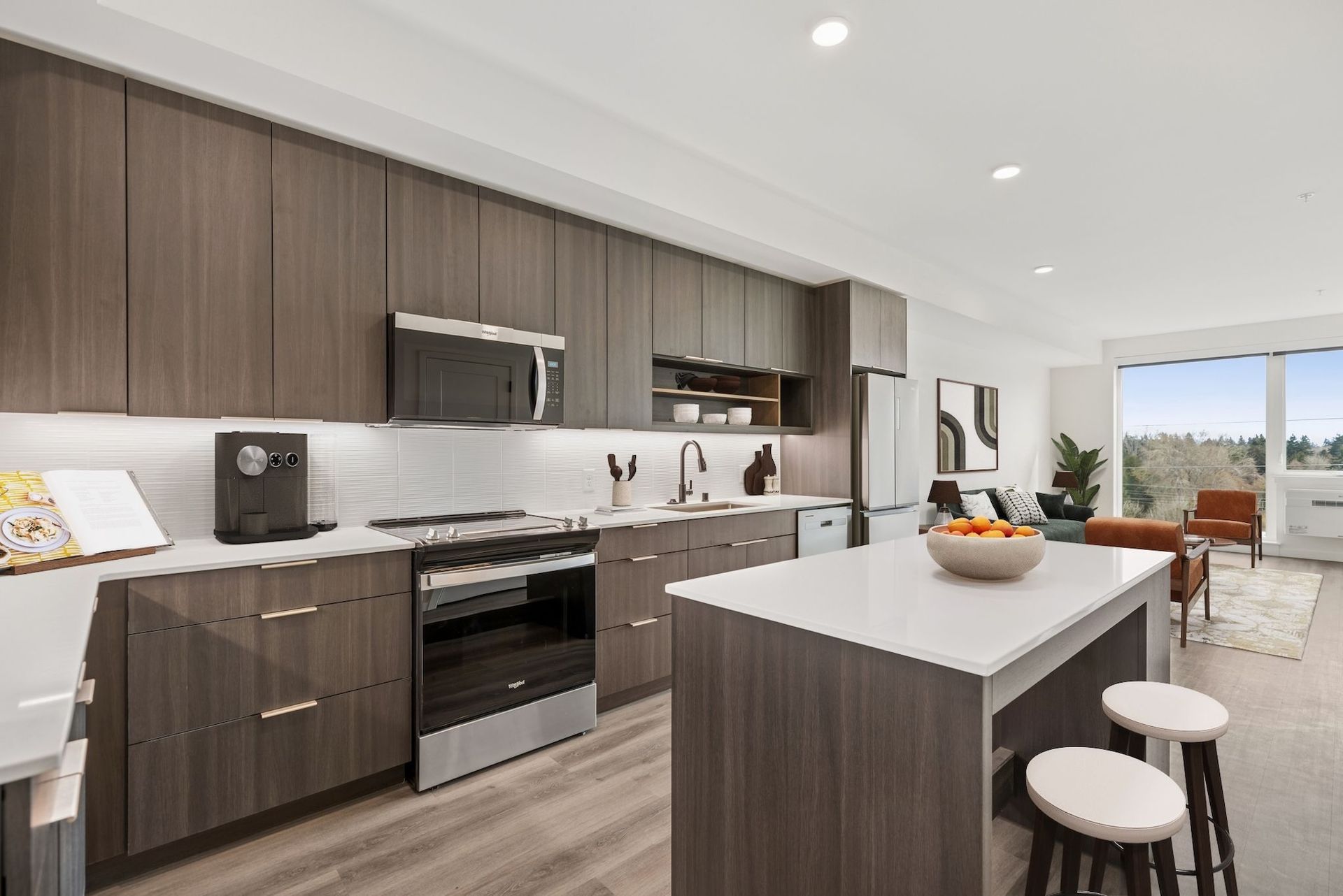 Modern kitchen with dark wood cabinets, white island, stainless appliances, and dining area by a bright window.