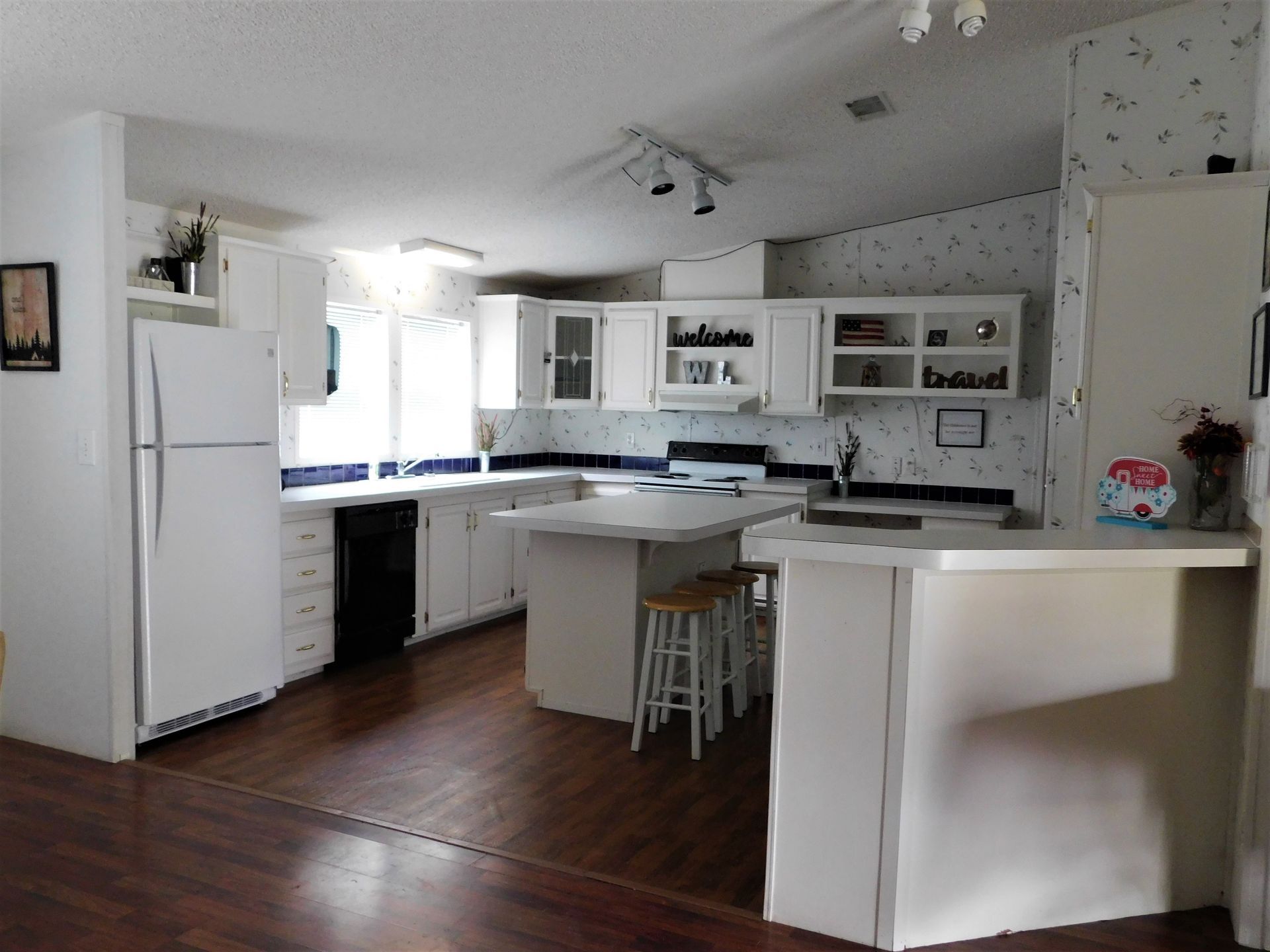 White kitchen with dark wood floors, white cabinets, and island with stools.
