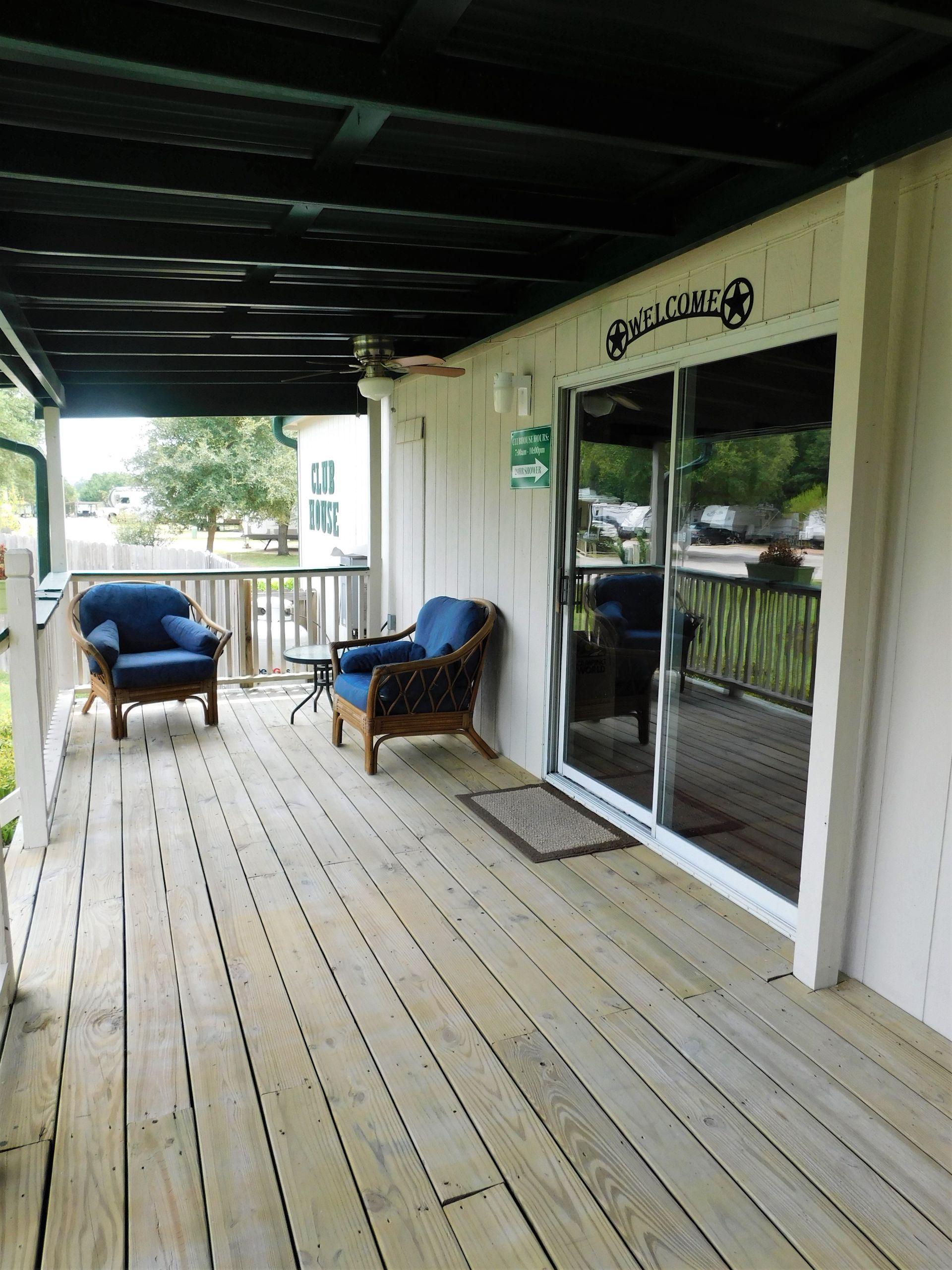 Covered porch with wood flooring, two blue chairs, and a sliding glass door.