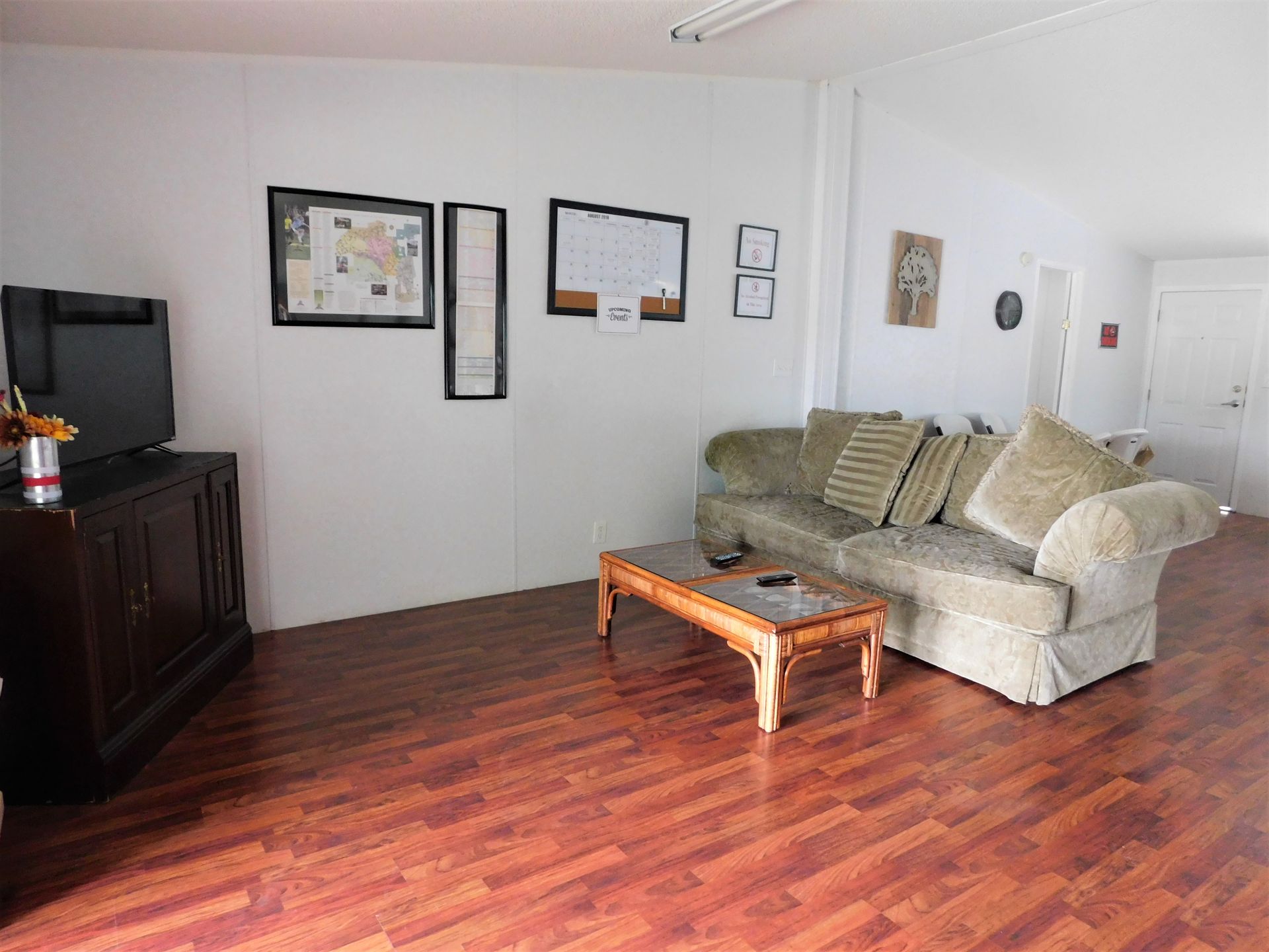 A living room with wooden floors, a couch, coffee table, TV and framed artwork on white walls.