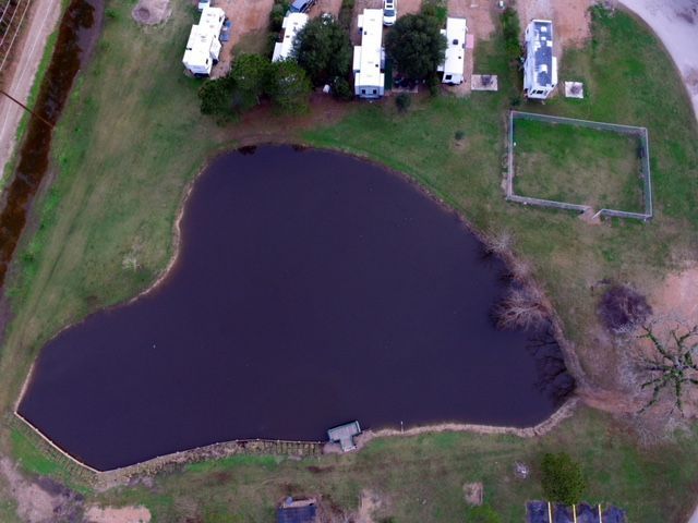 Aerial view of a heart-shaped pond surrounded by green grass, with RVs and a small fenced area.