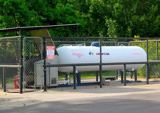 Propane tank behind a chain-link fence, under a metal roof, with warning sign.