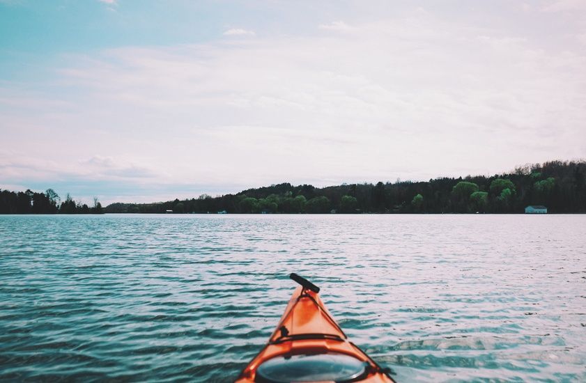 Orange kayak on blue water, view toward a tree-lined shore under a cloudy sky.