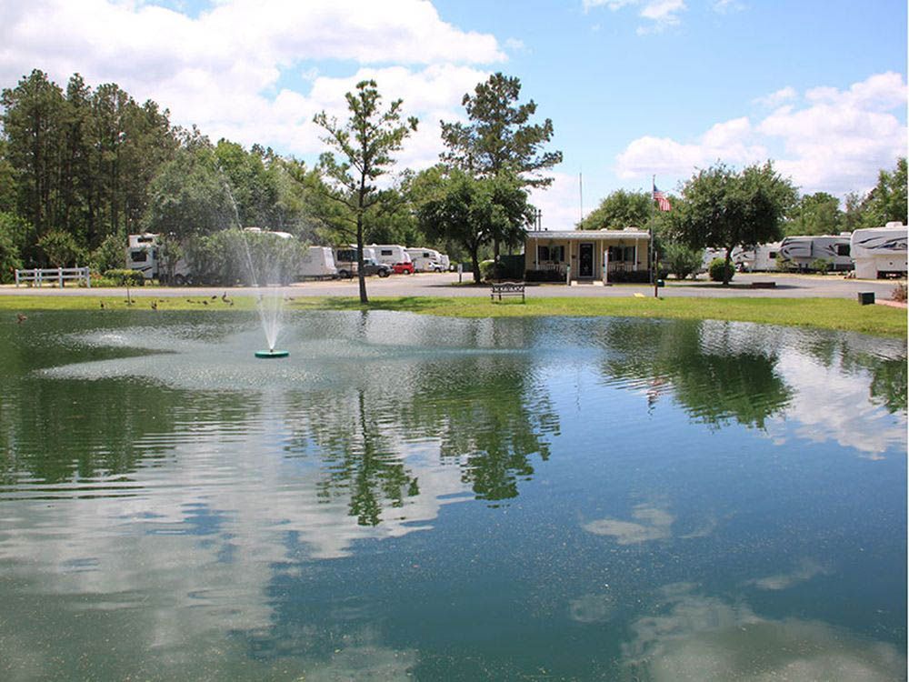 Pond with fountain in front of an RV park under a sunny sky.