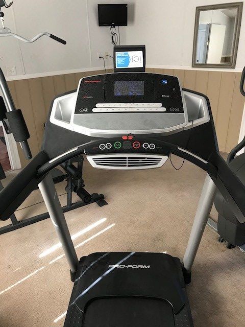 A black and silver Pro-Form treadmill in a home gym, with a small TV and mirror on the wall.