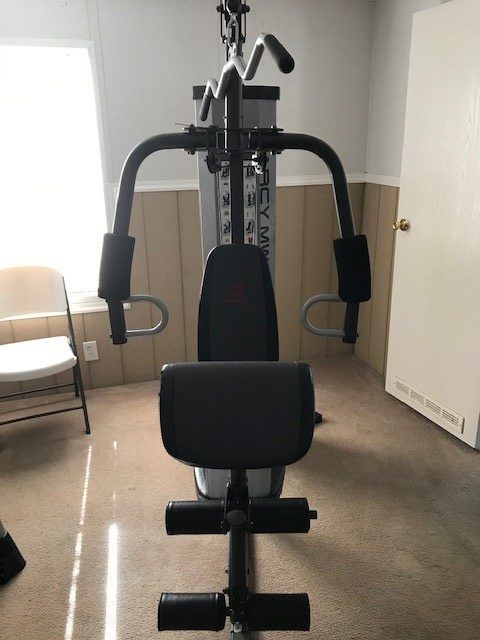 A home gym machine, black and gray, in a room with a chair and closed door.