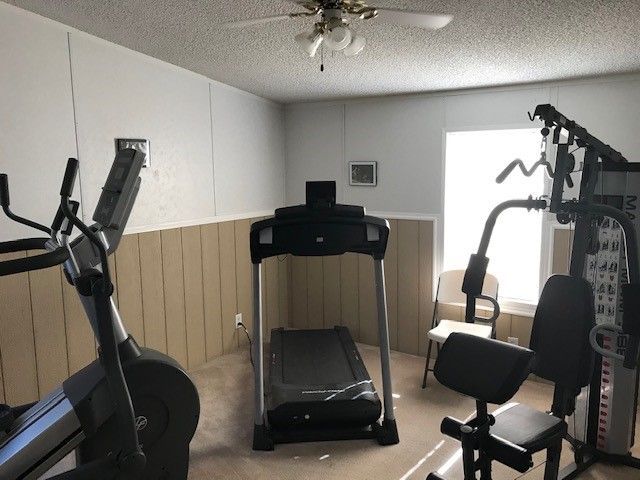 Home gym with treadmill, elliptical, multi-gym, and chair near a window.