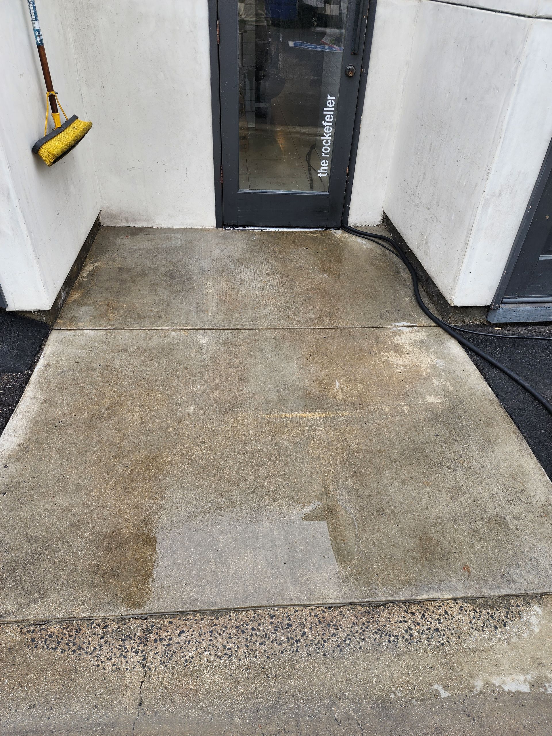 A dirty concrete walkway next to a door with a broom.