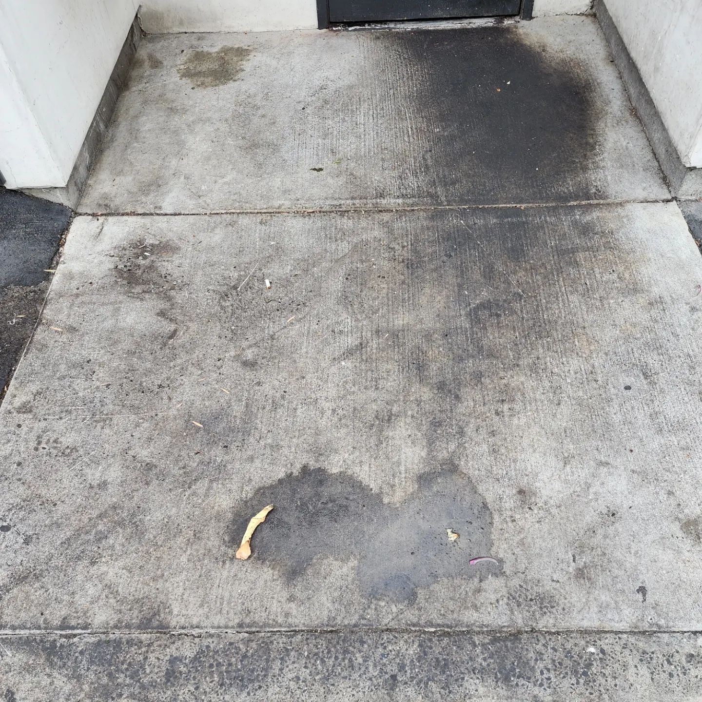 A dirty concrete walkway next to a building with a black door.