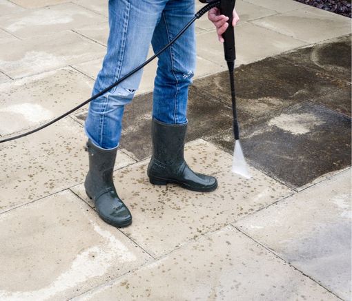A person is using a high pressure washer to clean a patio.