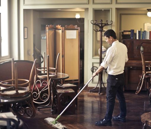 A man is mopping the floor in a room with tables and chairs