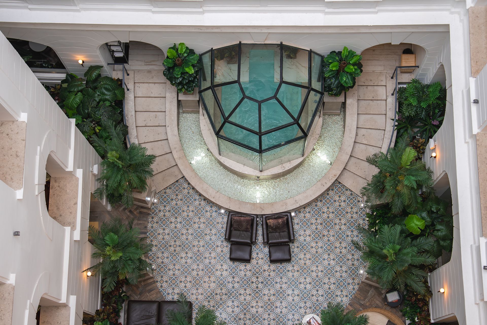 Top-down view of an interior courtyard with a glass-domed pool, patterned tile flooring, and potted plants.