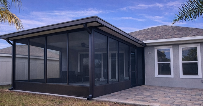 Screened patio enclosure attached to a gray house with stone pavers and a tiled roof.